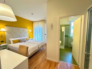Habitación de hotel con cama, mesitas de noche y un baño visible a través de una puerta abierta.