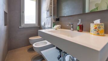 A modern bathroom with a large sink, two toilets, and a towel rack.
