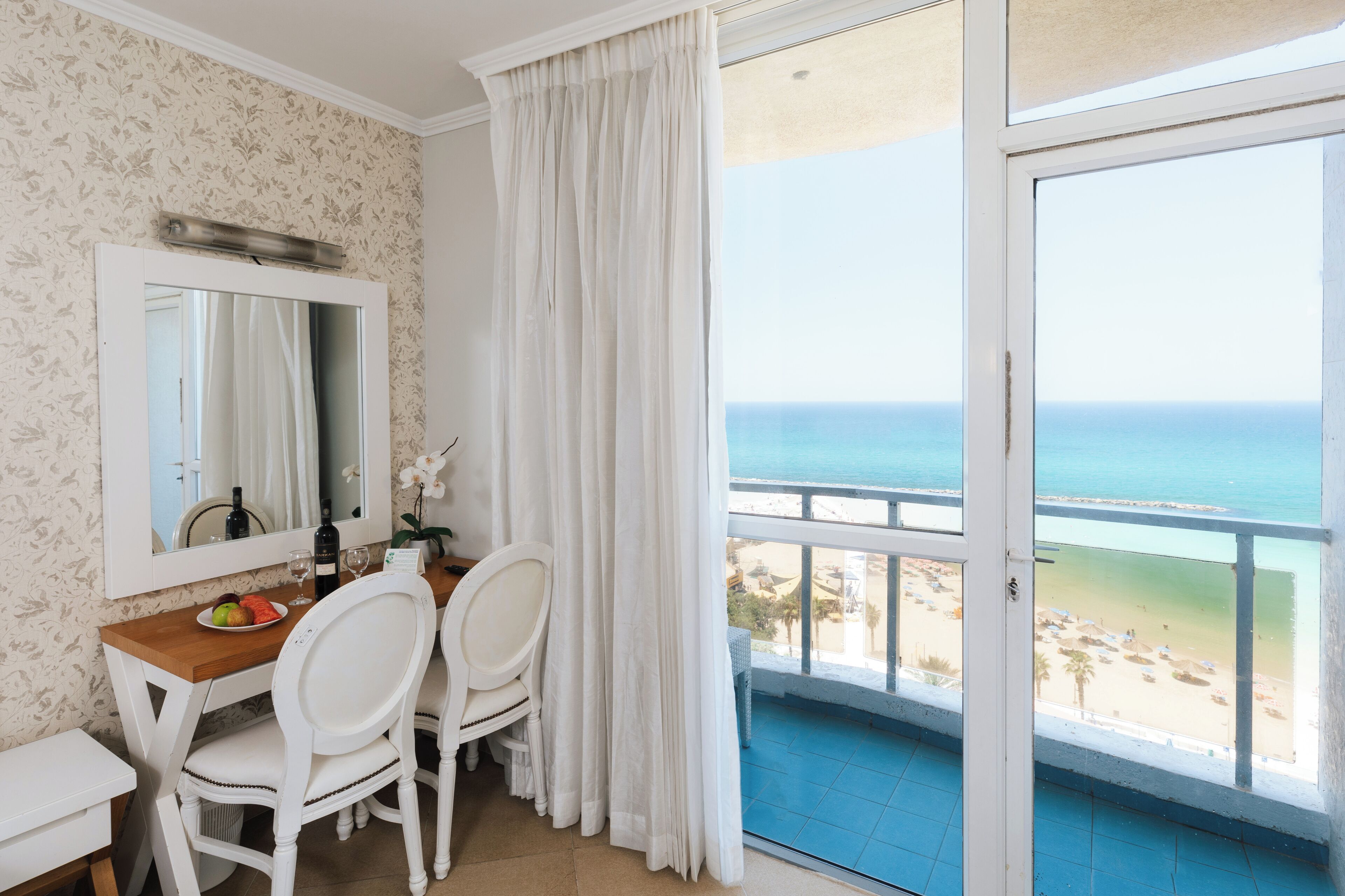 Una habitación con comedor, un ventanal con vista a la playa y un balcón con barandal azul.
