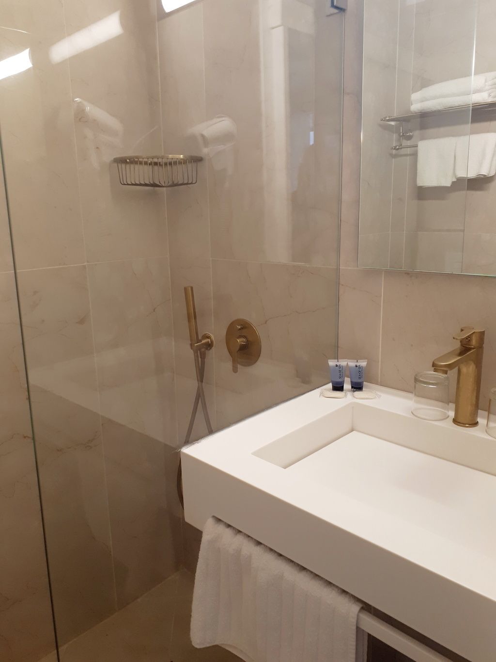 Un baño moderno con cabina de ducha de vidrio, un lavabo blanco y un grifo dorado.