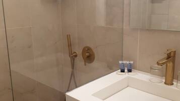 Un baño moderno con cabina de ducha de vidrio, un lavabo blanco y un grifo dorado.