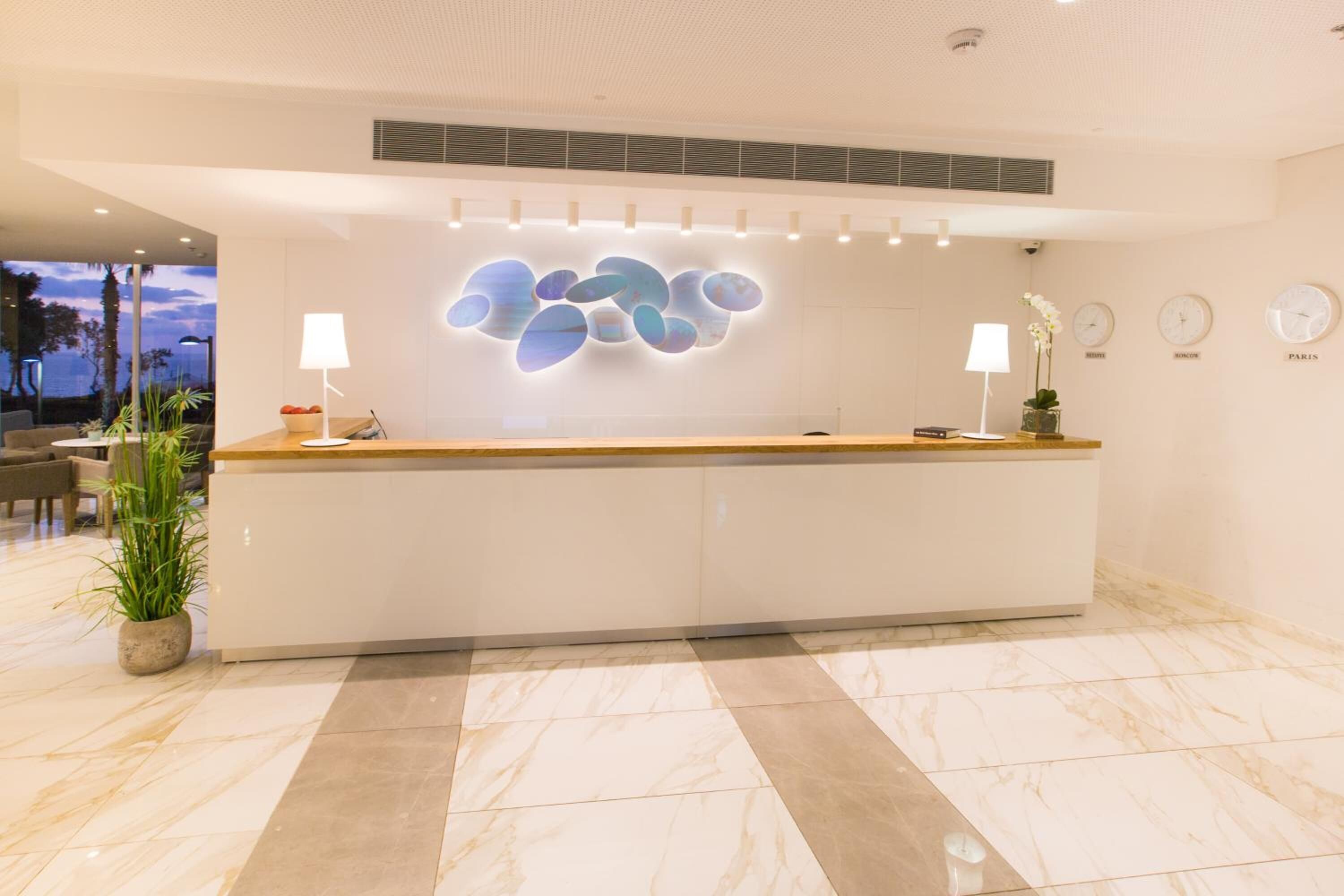 Un moderno mostrador de recepción con piso de mármol, dos lámparas de pared y una obra de arte decorativa.