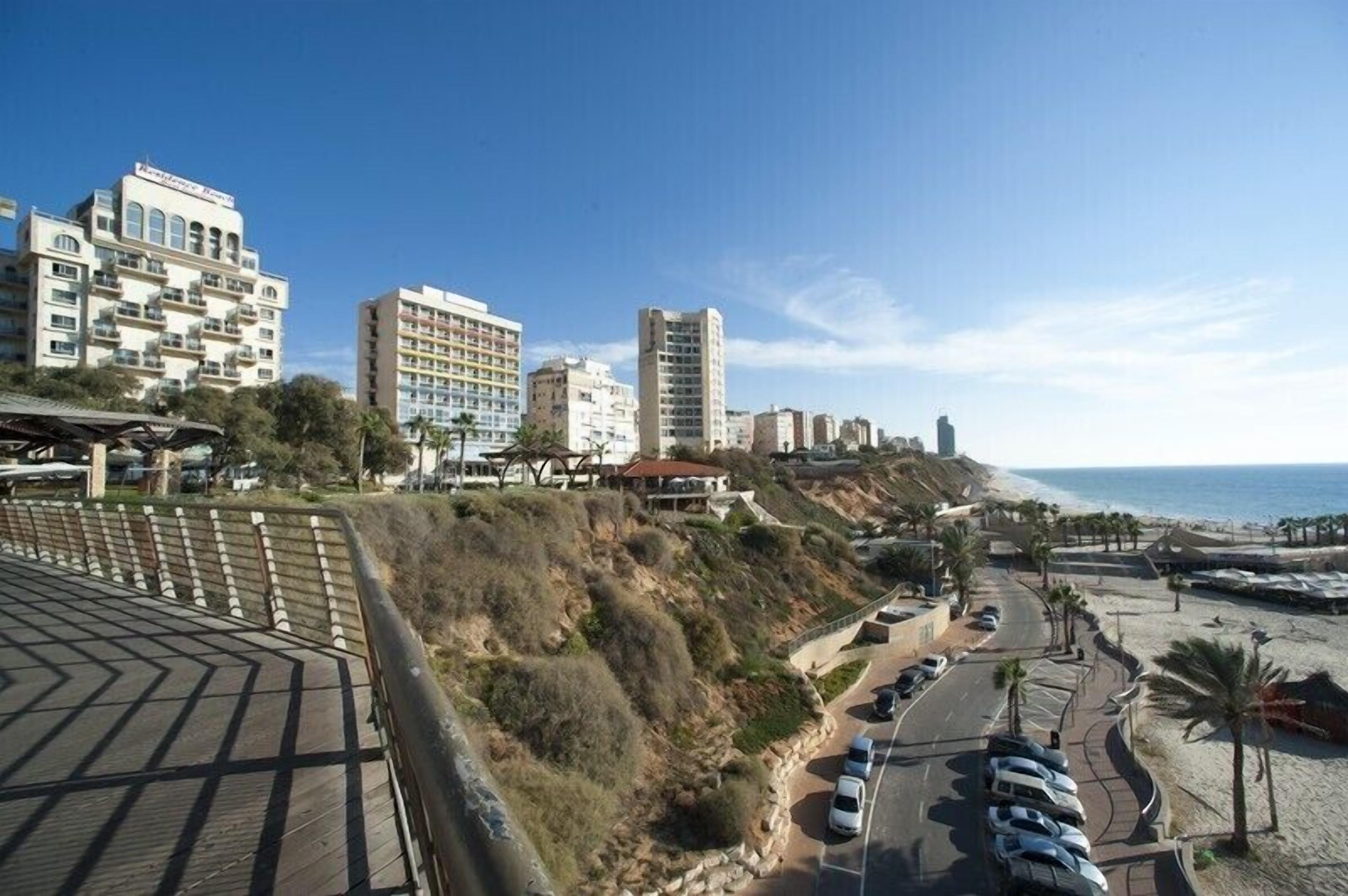 A coastal hotel with multiple buildings, a parking area, and a beach in the background.