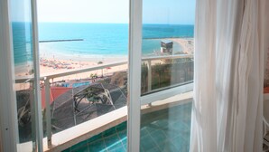Vista desde una ventana con vista a una playa, una piscina y un edificio a lo lejos.