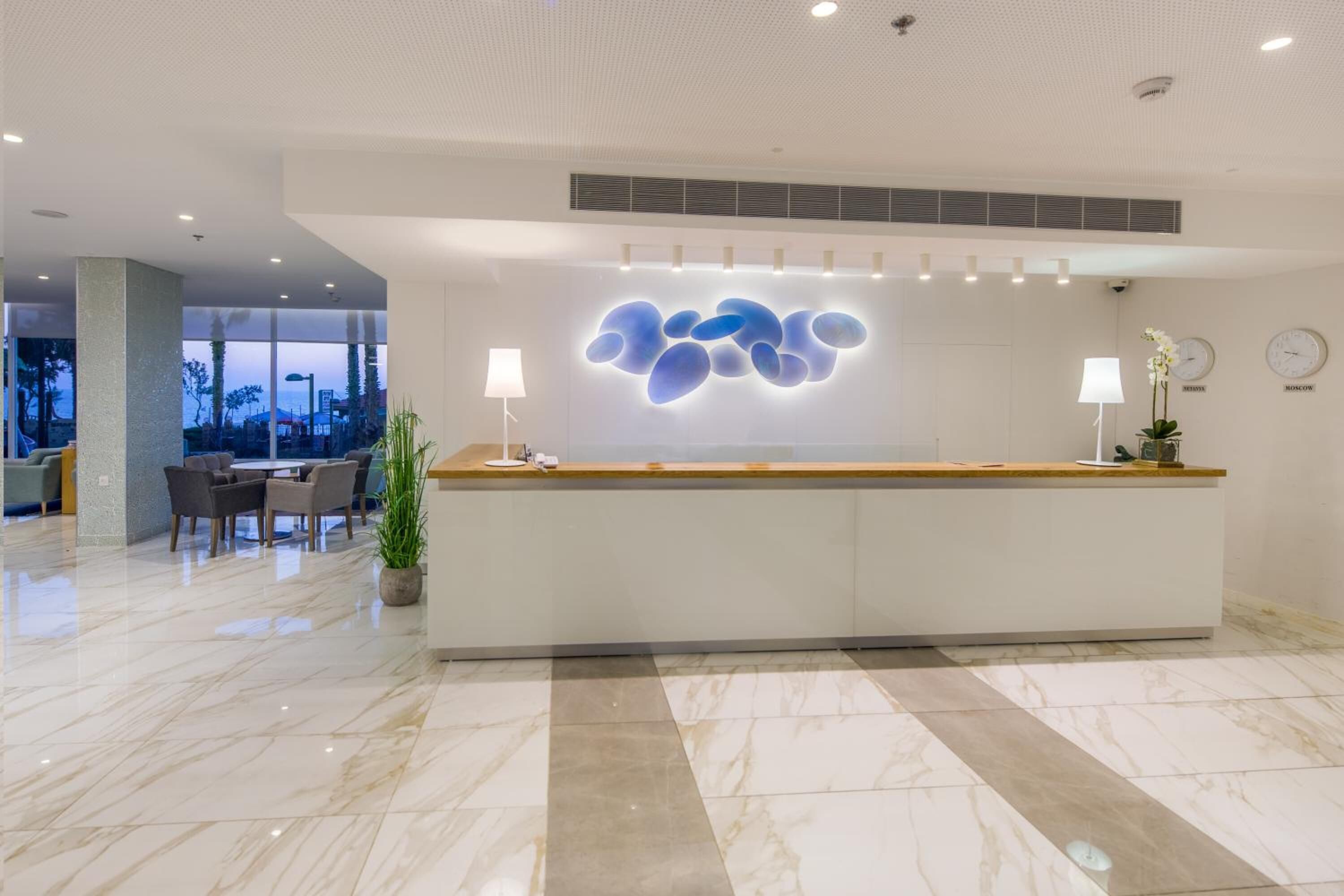 A modern hotel reception area with a marble floor, a reception desk, and a seating area with chairs and a table.