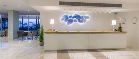 A modern hotel reception area with a marble floor, a reception desk, and a seating area with chairs and a table.