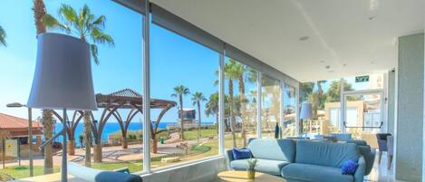 A modern living room with a large window overlooking a pool and palm trees, a sofa, a coffee table, and a lamp.