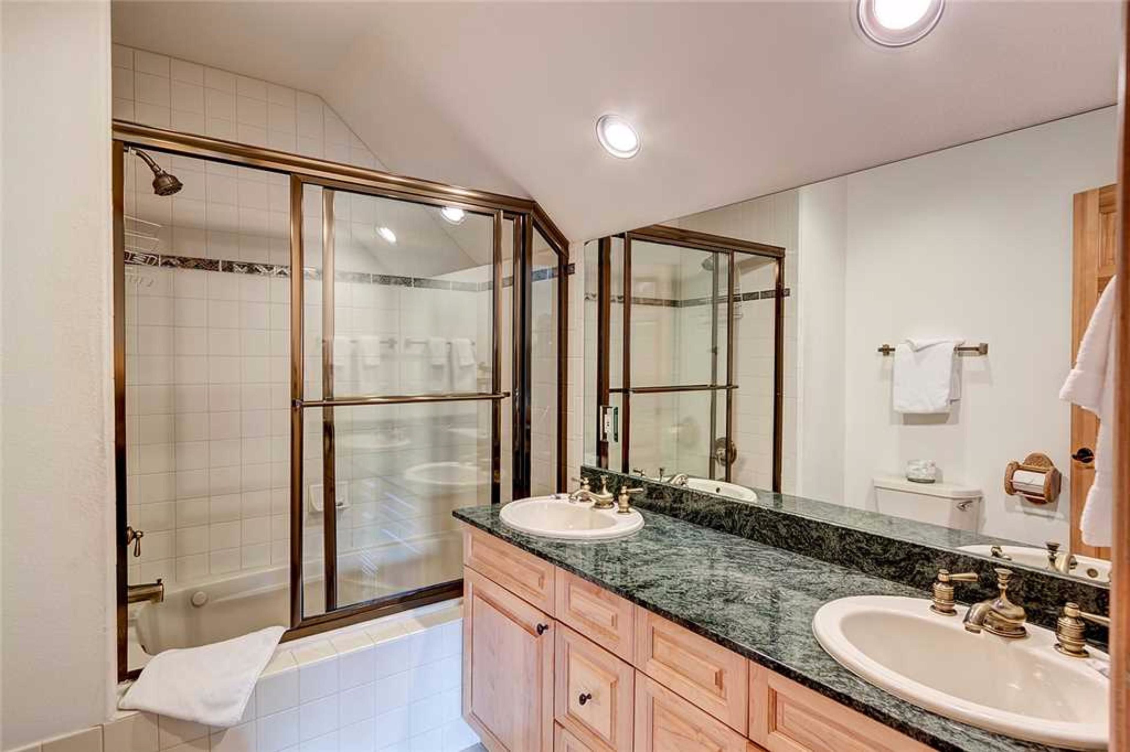 A modern bathroom with a glass-enclosed shower, two sinks with marble countertops, and a large mirror.