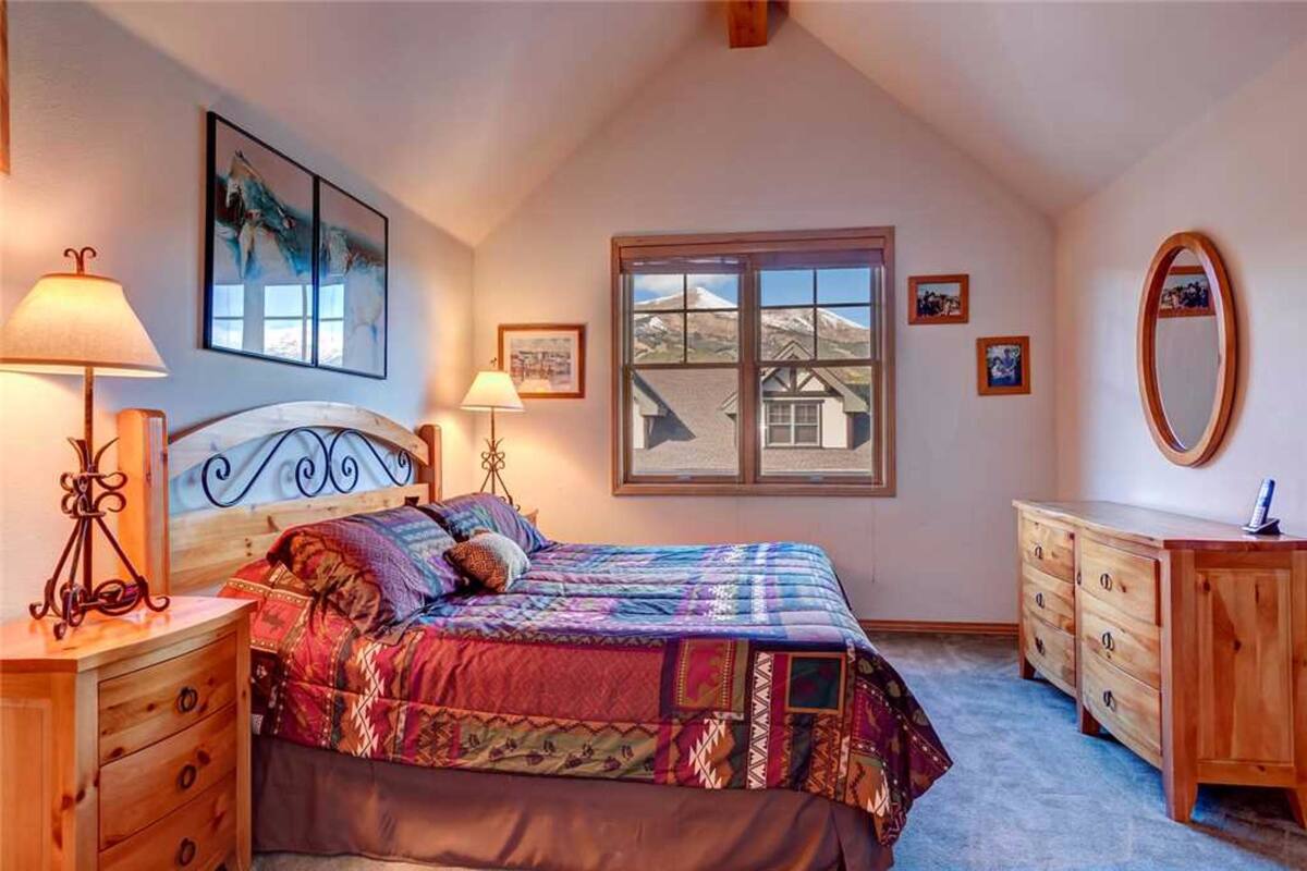 Ein Schlafzimmer mit einem Bett, zwei Nachttischen, einer Kommode, einem Fenster mit Ausblick und gerahmten Bildern an den Wänden.