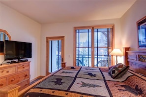 Een slaapkamer met een groot bed, een televisie op een houten dressoir en een raam met zonwering.