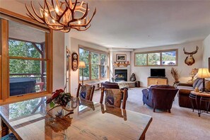 A spacious living room with a fireplace, large windows, and rustic decor including antler chandeliers. - The Corral at Breckenridge by Great Western Lodging (Breckenridge)