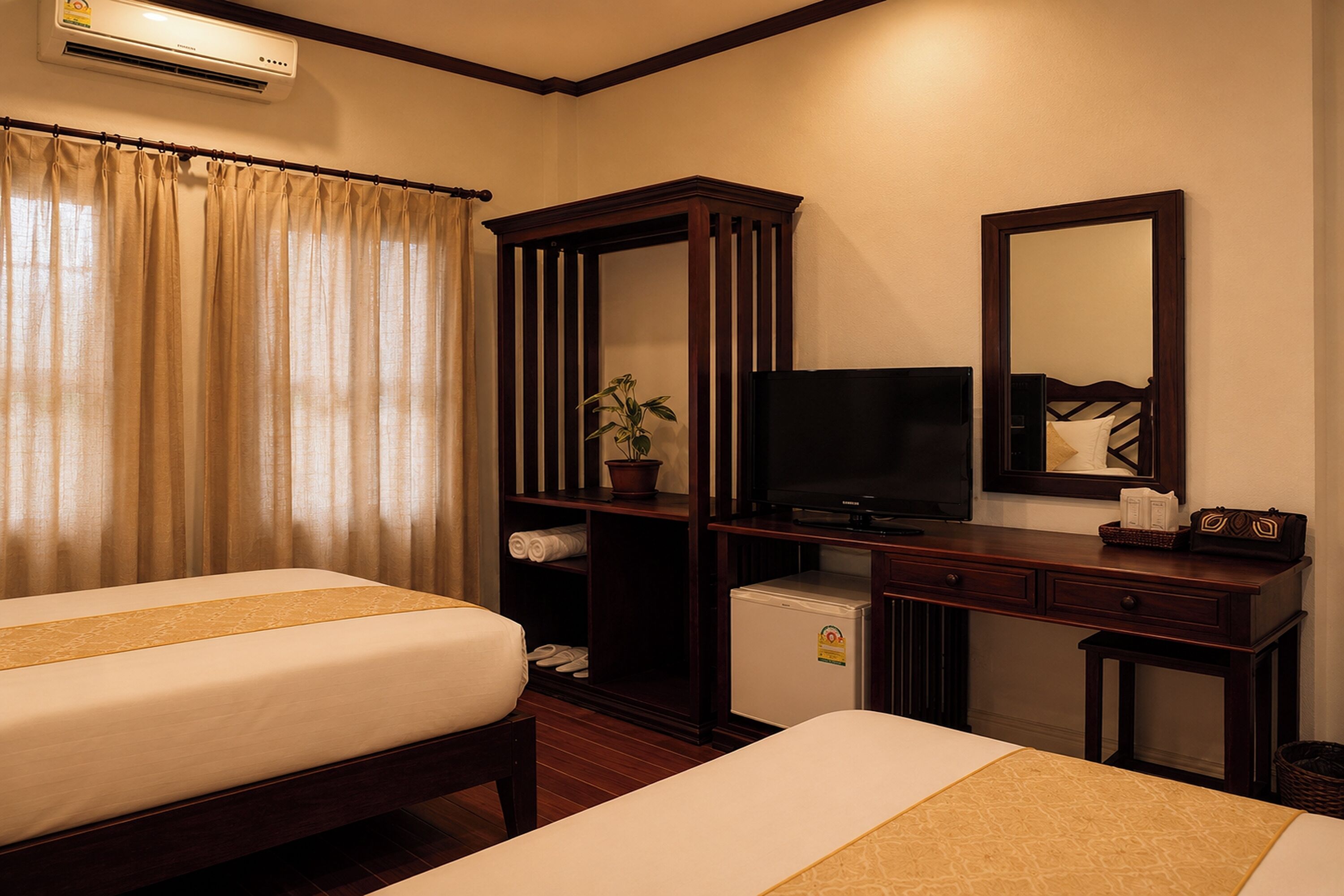 A hotel room with two beds, a television, a wardrobe, a desk, and a small refrigerator.