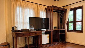 Una stanza con una scrivania in legno, una televisione, un piccolo frigorifero e una finestra con tende.