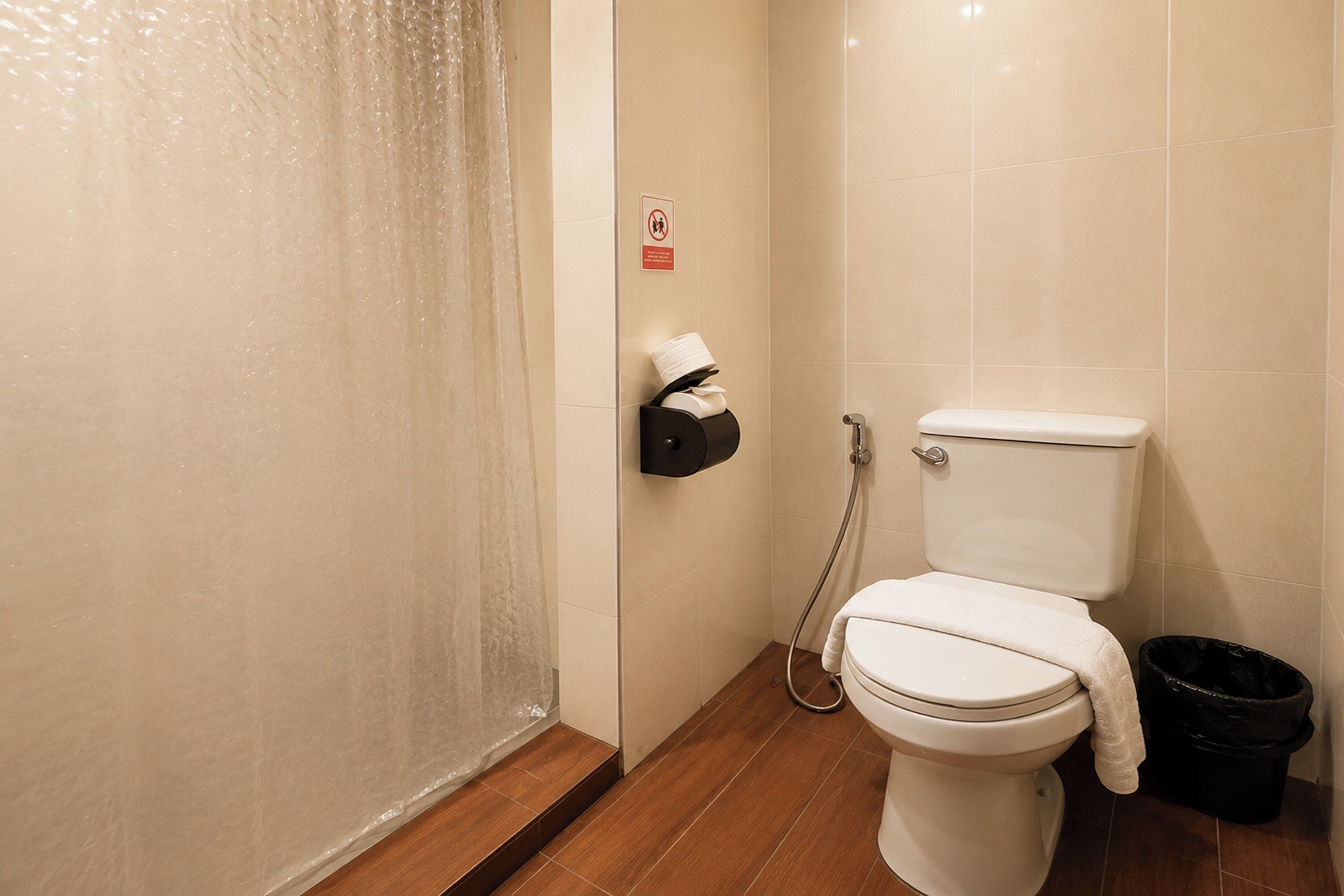 A bathroom with a toilet, a shower curtain, a towel dispenser, and a trash bin.