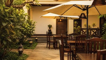 Un área de comedor al aire libre con mesas y sillas de madera, sombrillas y faroles decorativos.