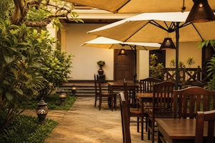 An outdoor dining area with wooden tables and chairs, umbrellas, and decorative lanterns.