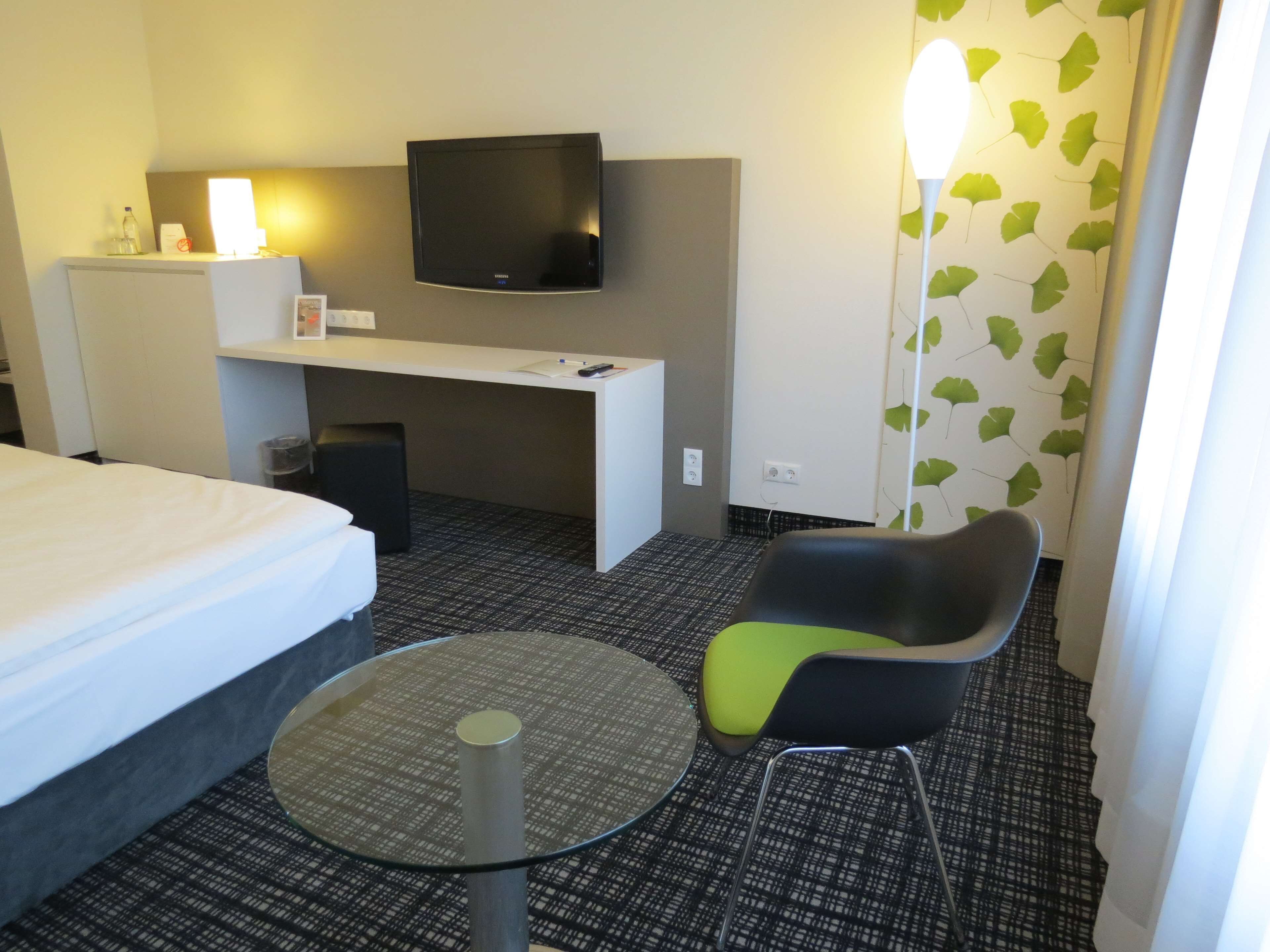 Une chambre d’hôtel comprenant un lit, un bureau avec un téléviseur à écran plat, une chaise et une petite table.