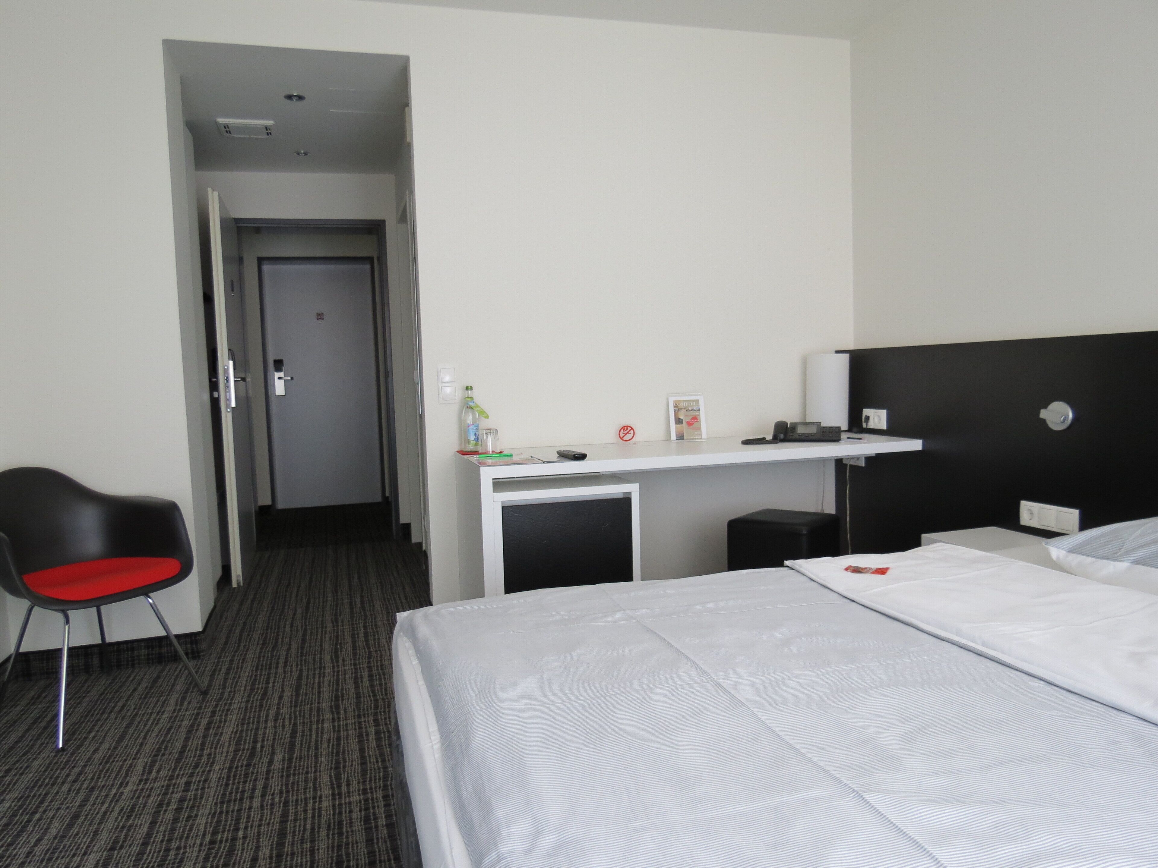 Ein Hotelzimmer mit einem Bett, einem Schreibtisch mit Computer, einem Stuhl und einem kleinen Hocker.