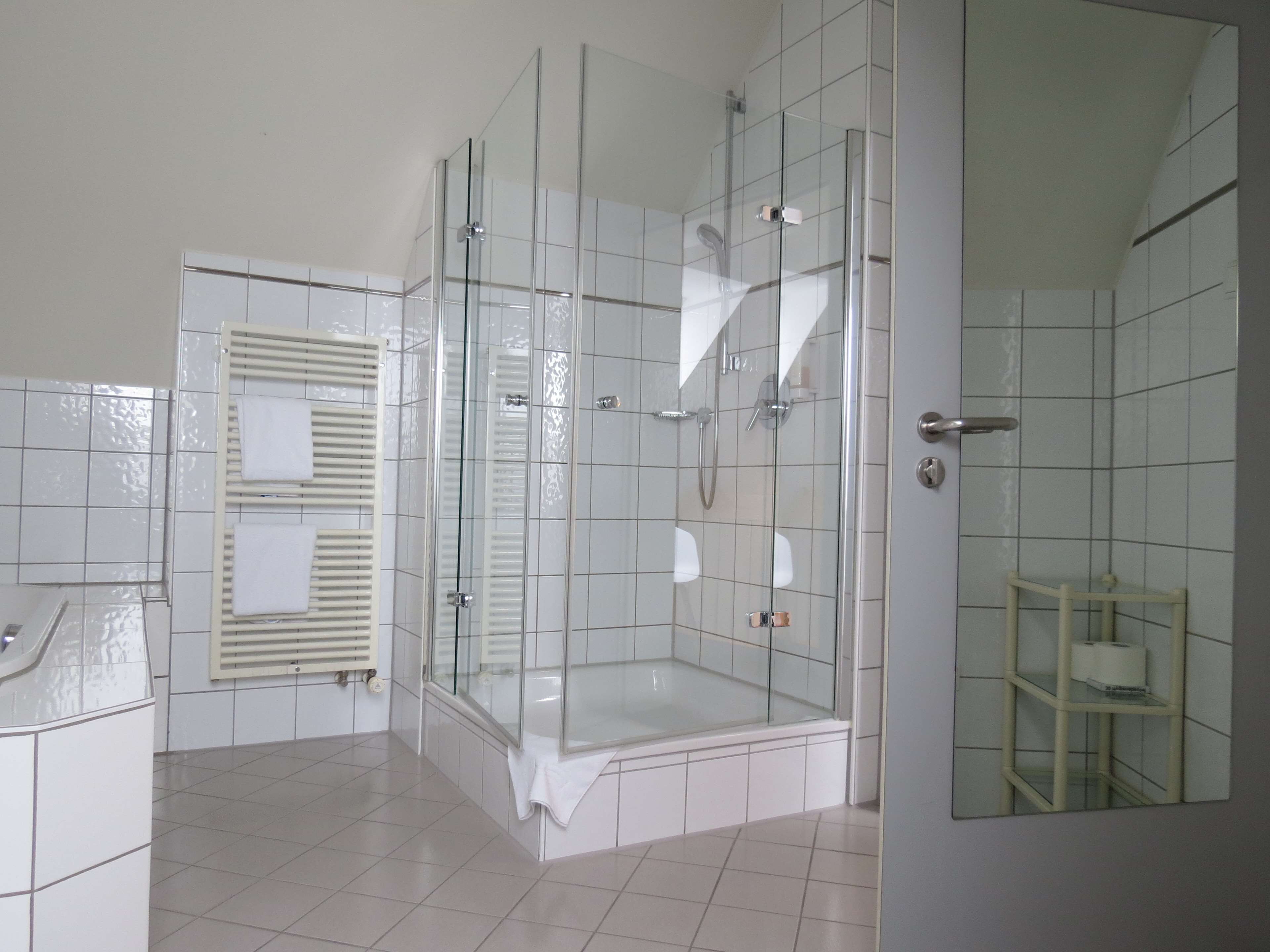 Un baño moderno con cabina de ducha de vidrio, paredes de azulejos blancos y un pequeño estante con artículos de aseo.