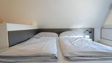 Una cama con dos plazas, un cabecero gris y ropa de cama blanca en una habitación con techo inclinado.