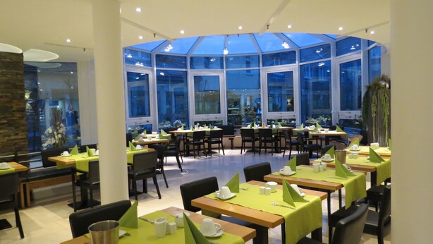 A restaurant with multiple tables, green tablecloths, and chairs. - Comfor Hotel Ulm City (Ulm)