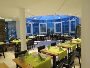 Un restaurante con varias mesas, manteles verdes y sillas.