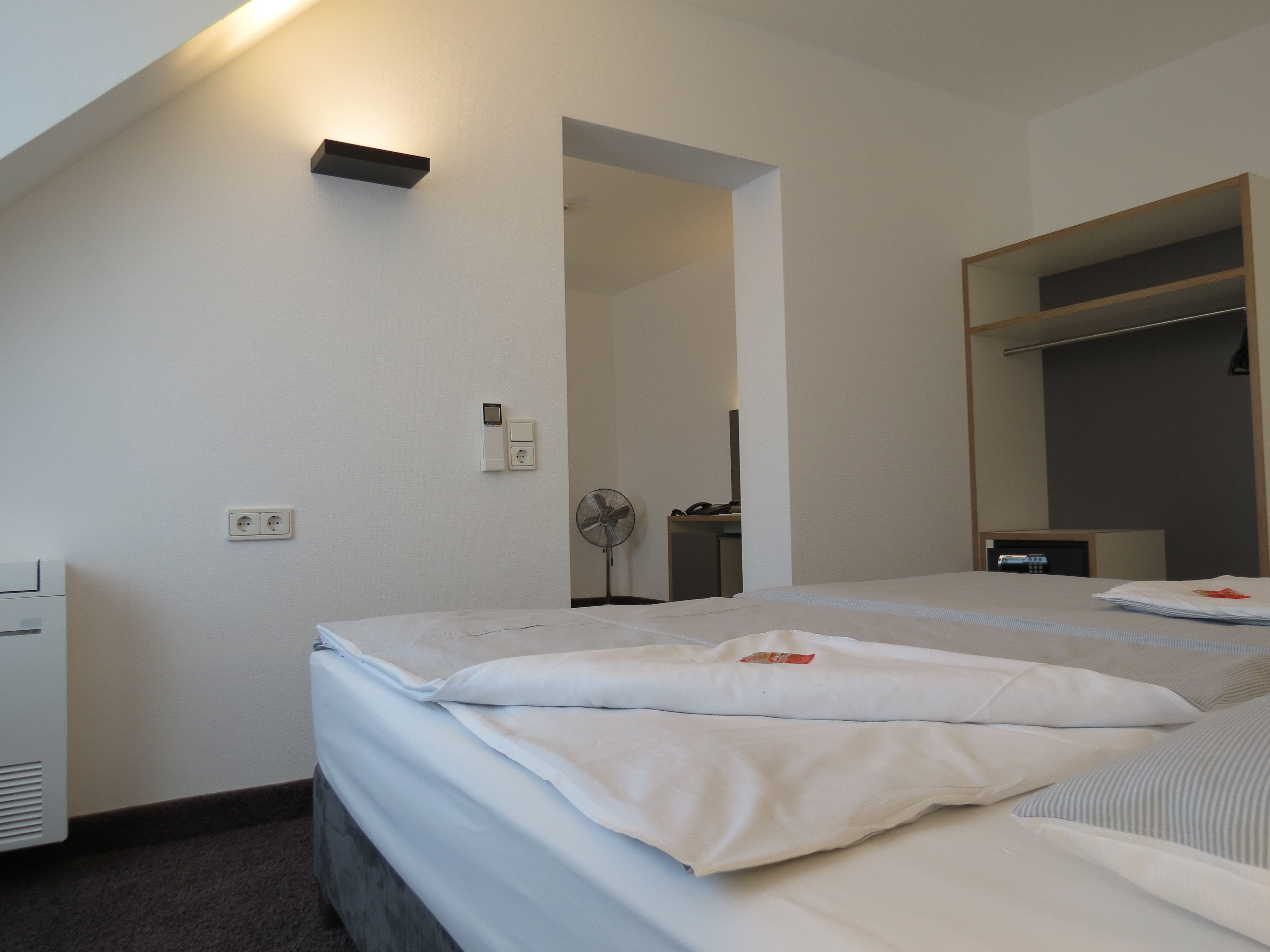 Habitación de hotel con dos camas, una mesita de noche, un espejo, un armario y un ventilador de pie.