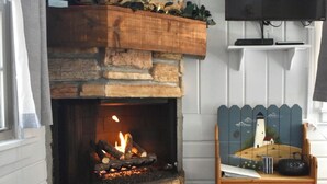 A cozy living room with a stone fireplace, a television mounted on the wall, and a wooden bench with a decorative item on it. - Lazy Cloud (Lake Geneva)