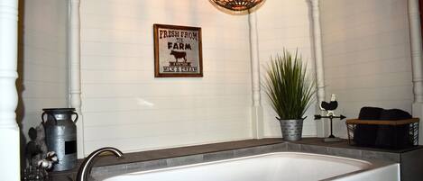 A bathroom with a large bathtub, a hanging light fixture, and a wall-mounted sign that reads "FRESH FROM THE FARM MILK & CREAM".