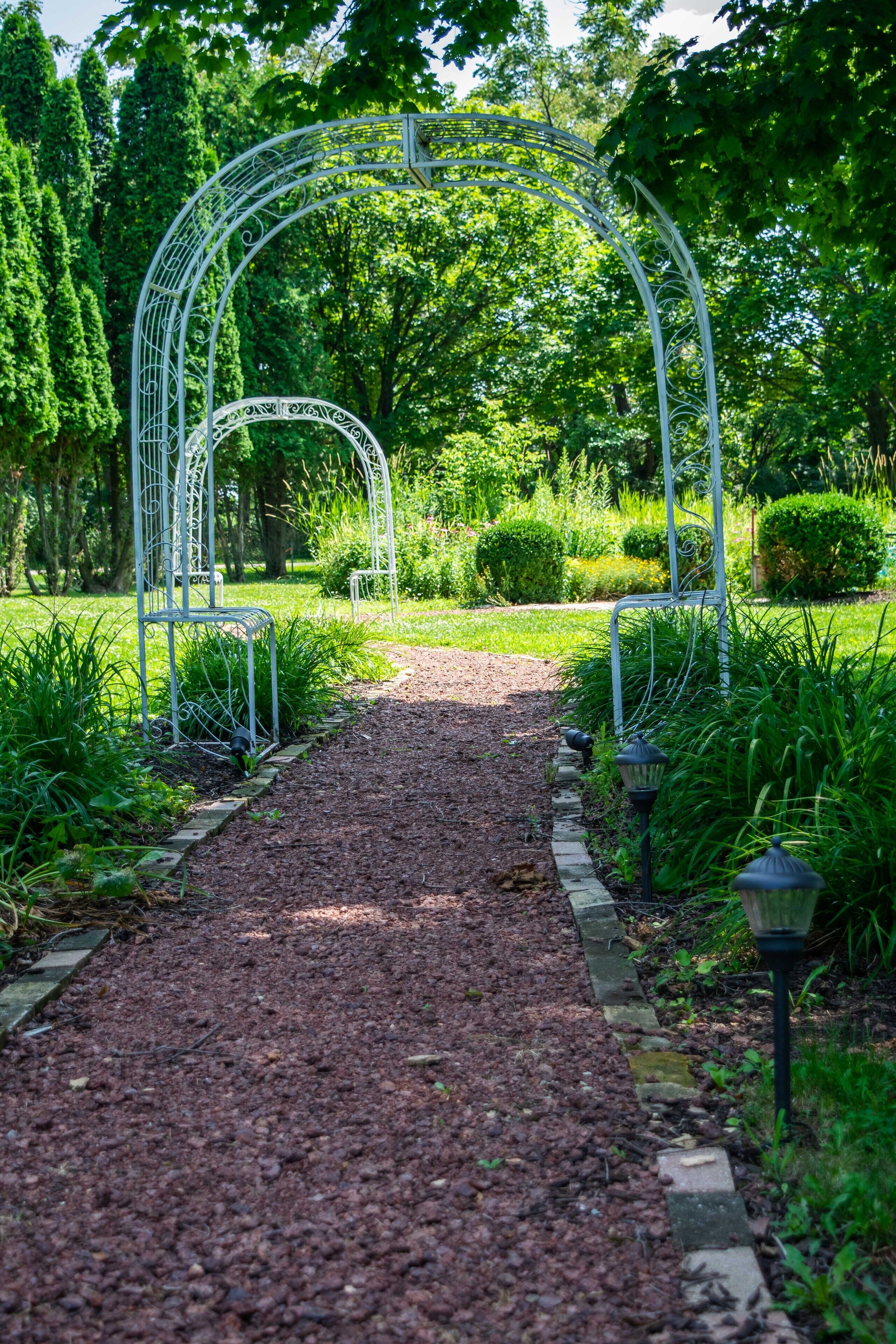 Un sentier de jardin agrémenté d’arceaux en métal et d’un chemin de gravier.