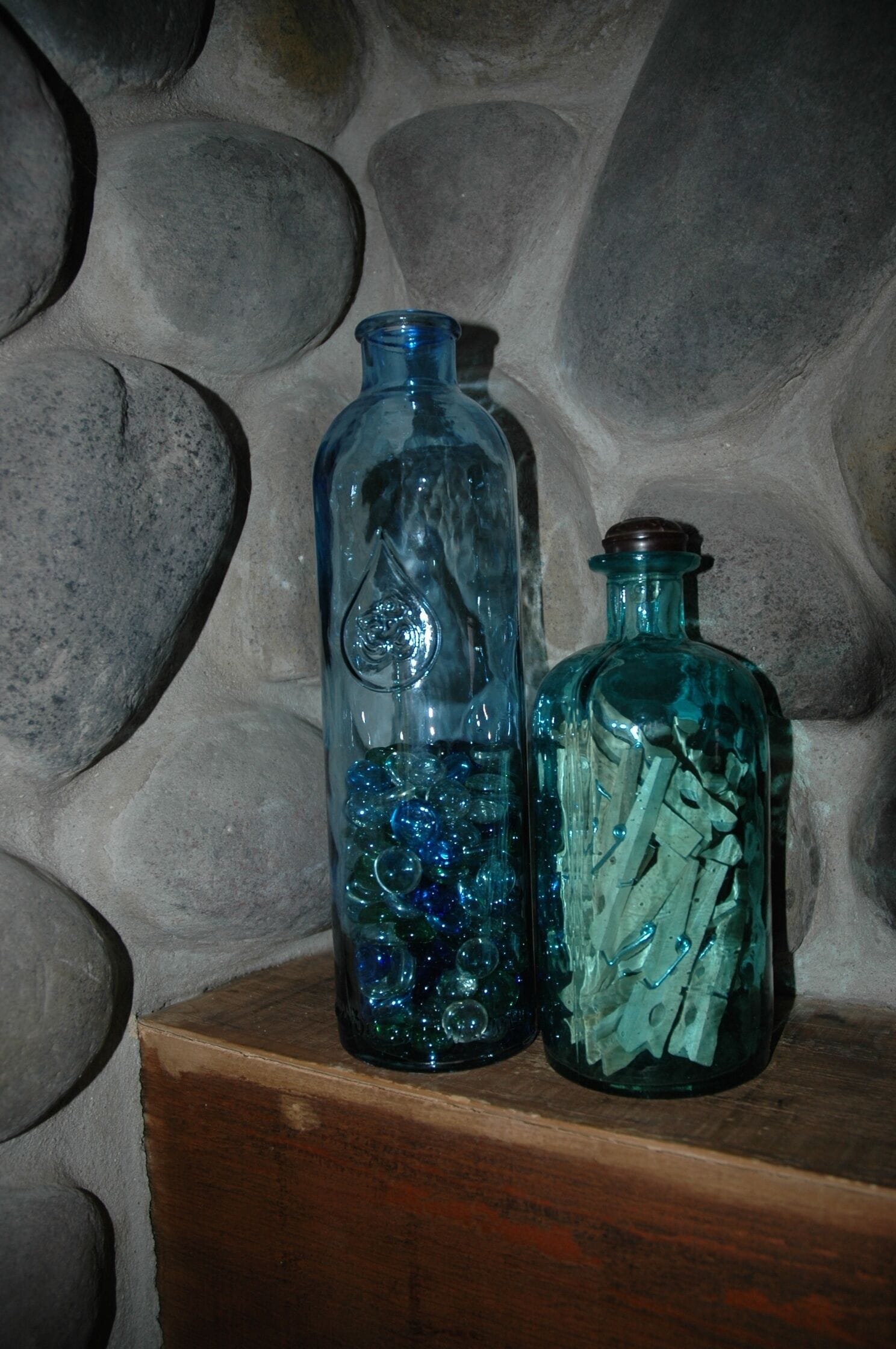 Two glass bottles with different contents on a wooden shelf against a stone wall.