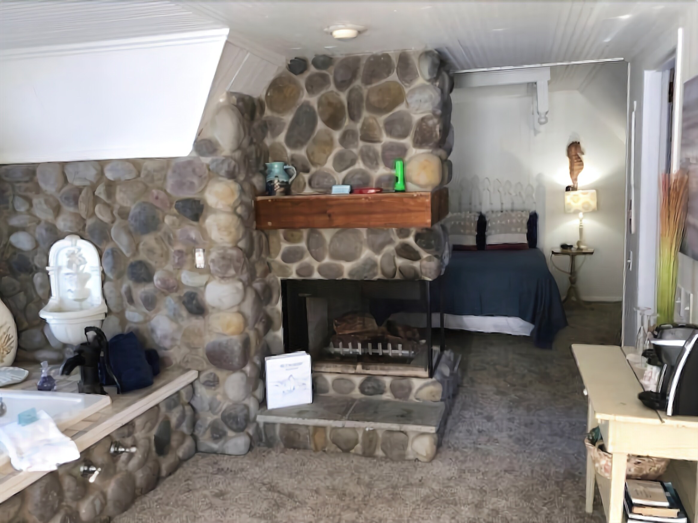 A cozy room with a stone fireplace, a bed, a nightstand, and a lamp.