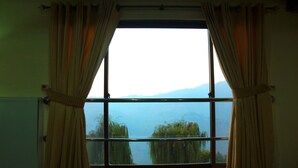 Una habitación con un ventanal amplio, cortinas y vistas a un cuerpo de agua y montañas.