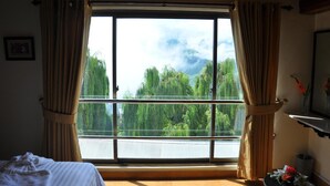 Una habitación con un ventanal grande, cortinas, una cama y una mesita con flores.