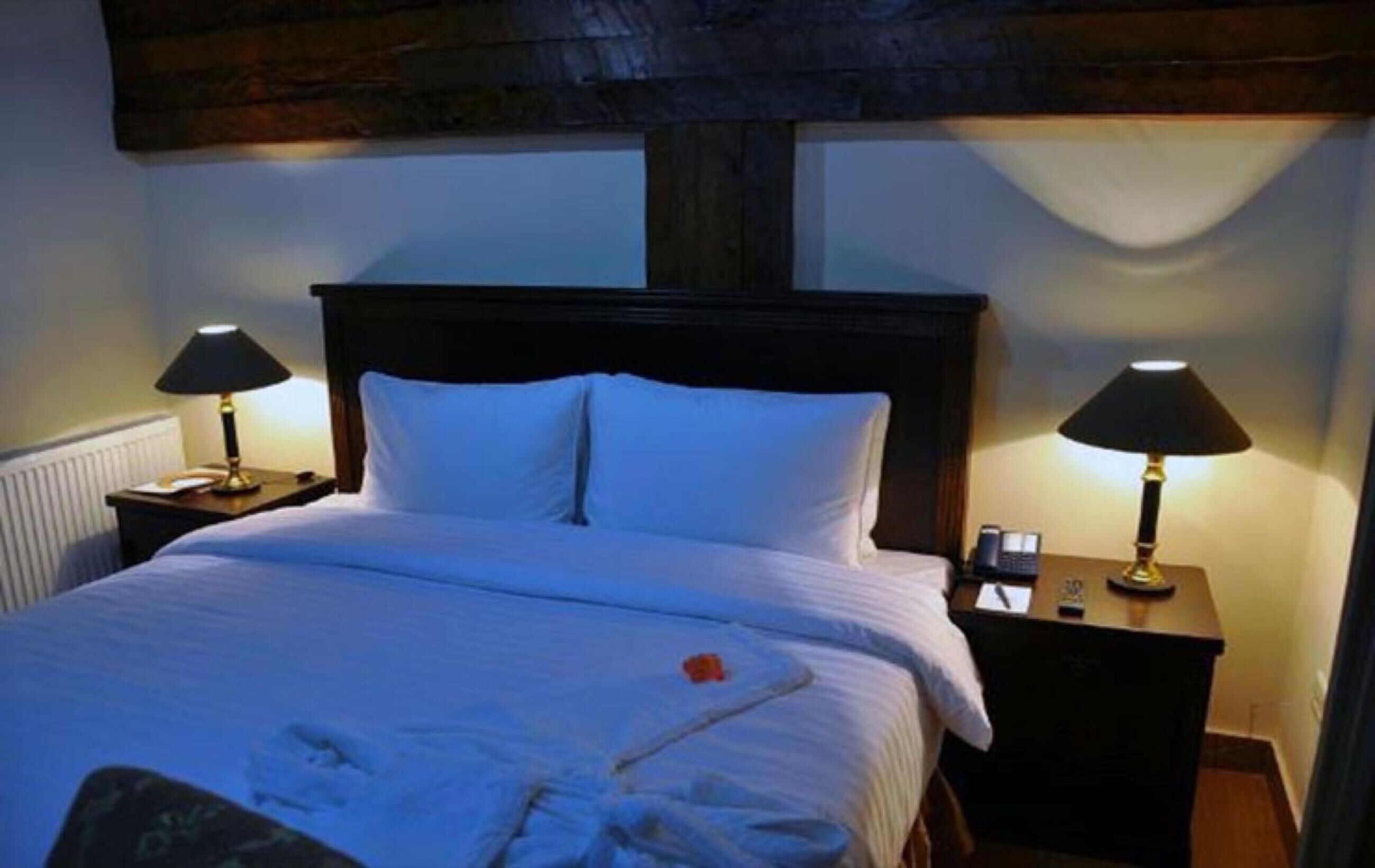 Una cama bien hecha con sábanas blancas y dos lámparas de noche.