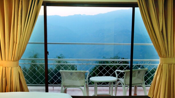 Un balcón con vistas a las montañas, una cama y dos sillas.