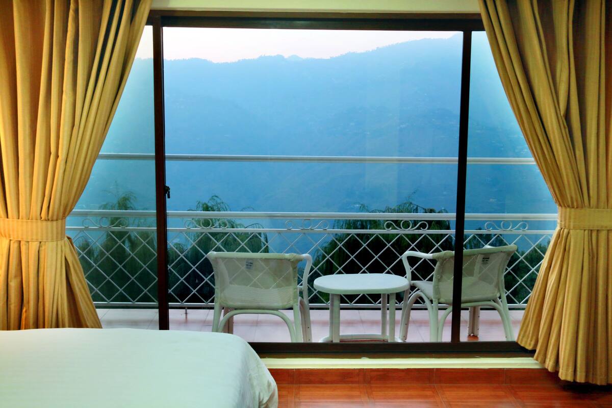 A balcony with a view of mountains, a bed, and two chairs.