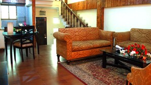 Una sala de estar con un sofá, una mesa de centro y una mesa de comedor con sillas. Se ve una escalera al fondo.
