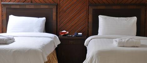 A hotel room with two beds, wooden paneling on the walls, and a nightstand between the beds.