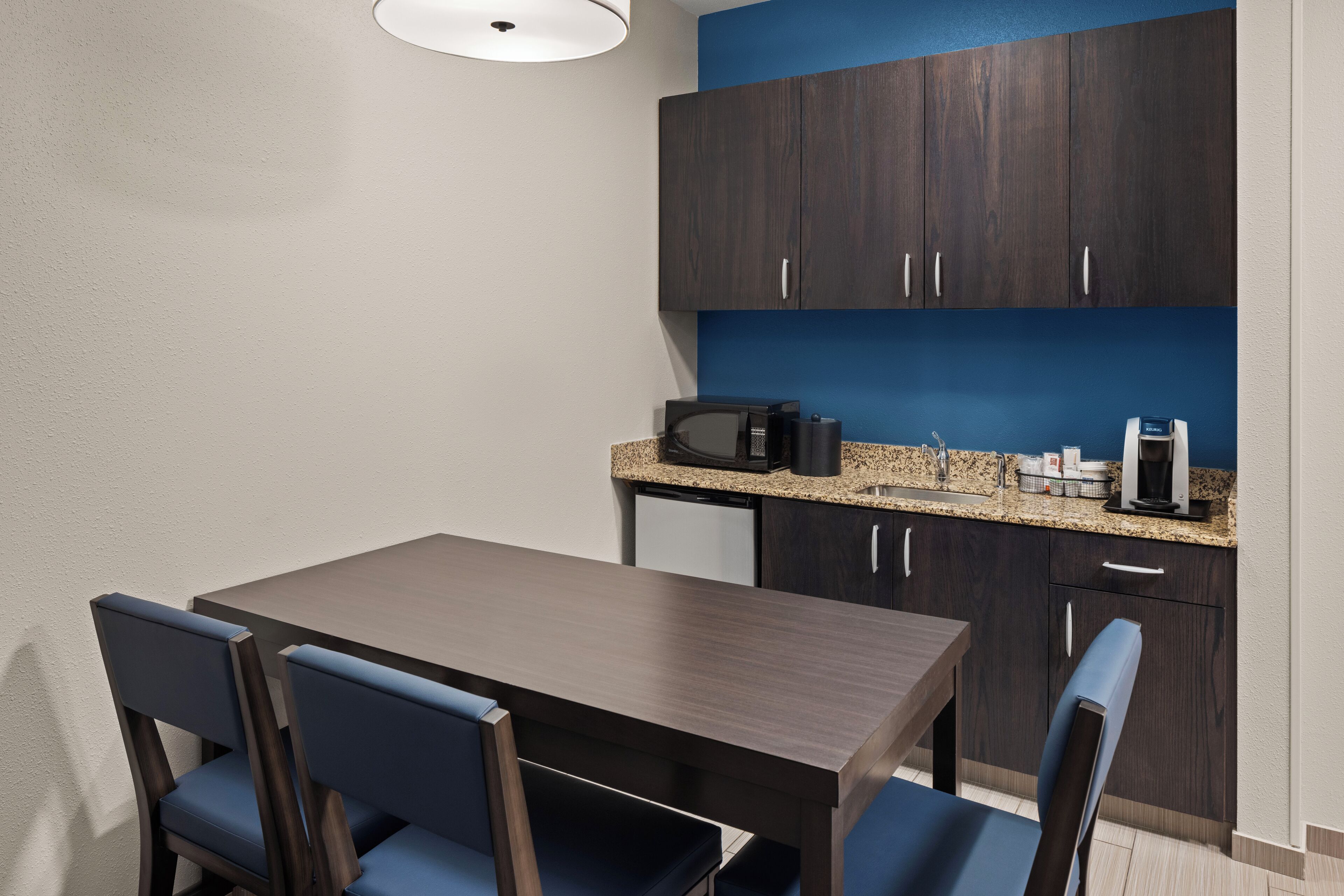 A modern kitchen with dark wooden cabinets, a granite countertop, and a coffee machine.