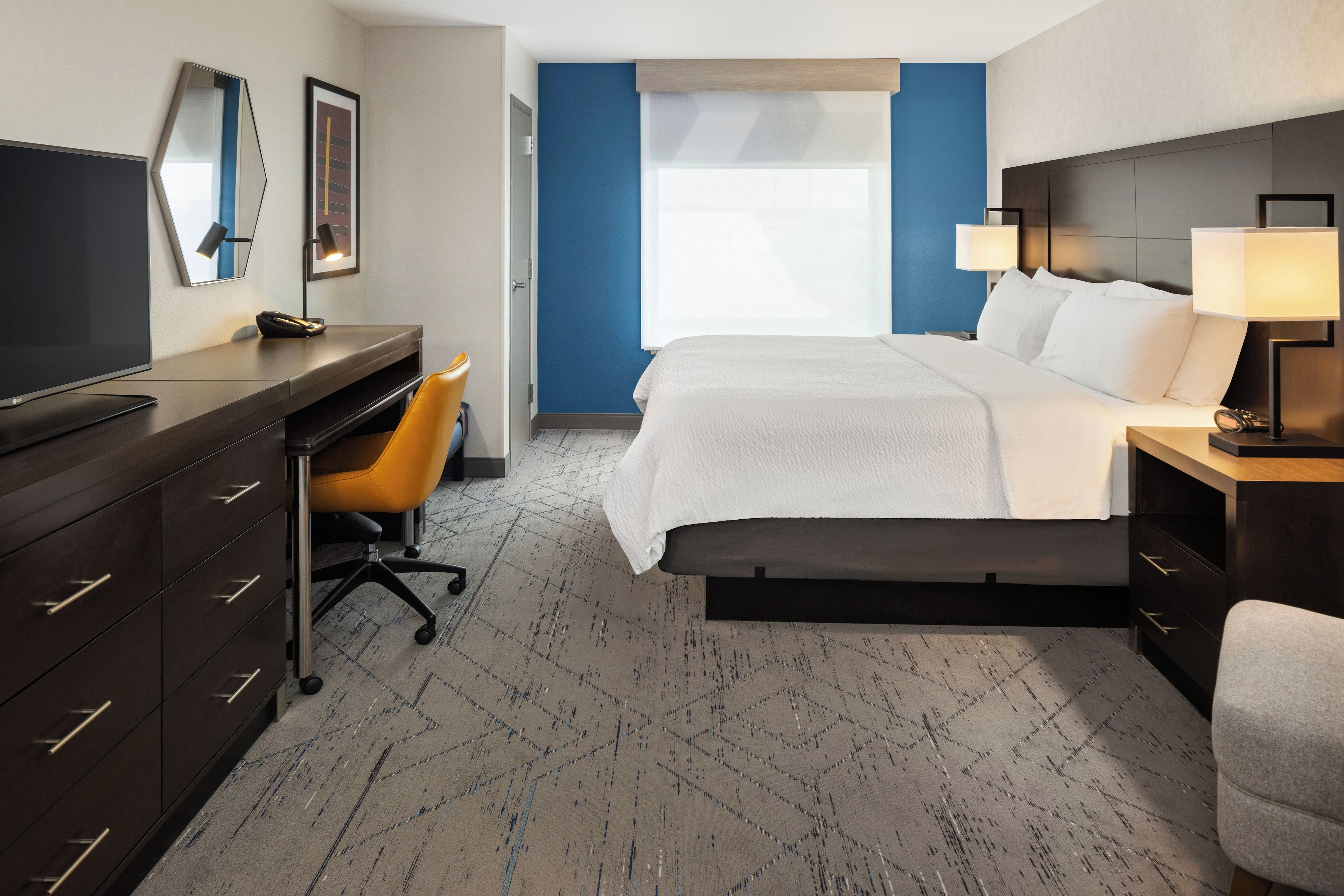 A hotel room with a bed, desk, chair, and a television.