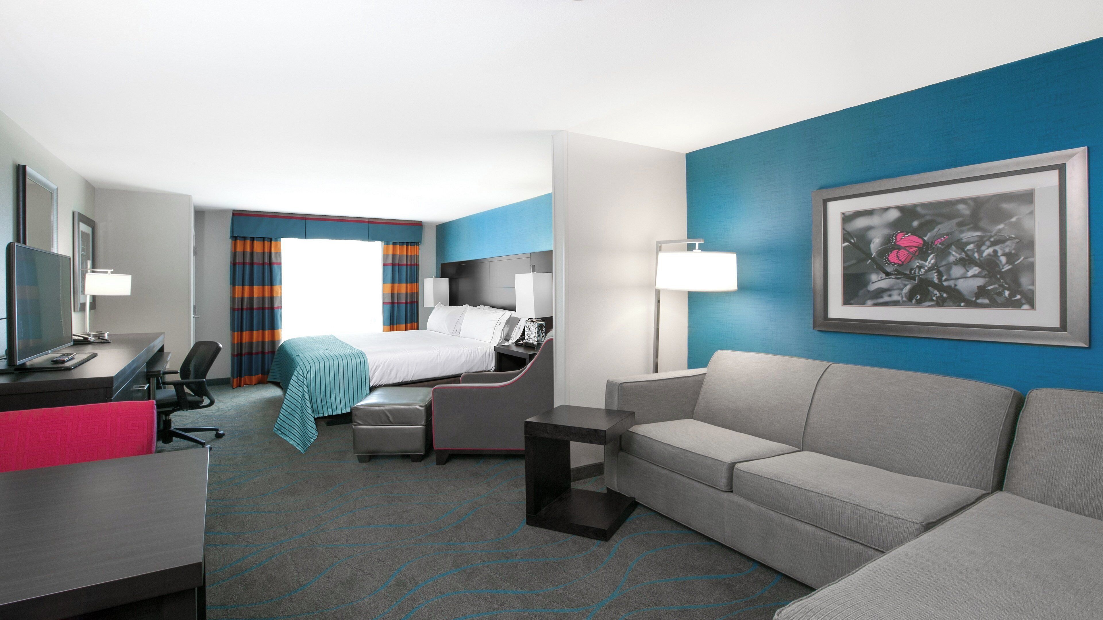 Una habitación de hotel con una cama, un escritorio con una computadora, un sofá y una silla.