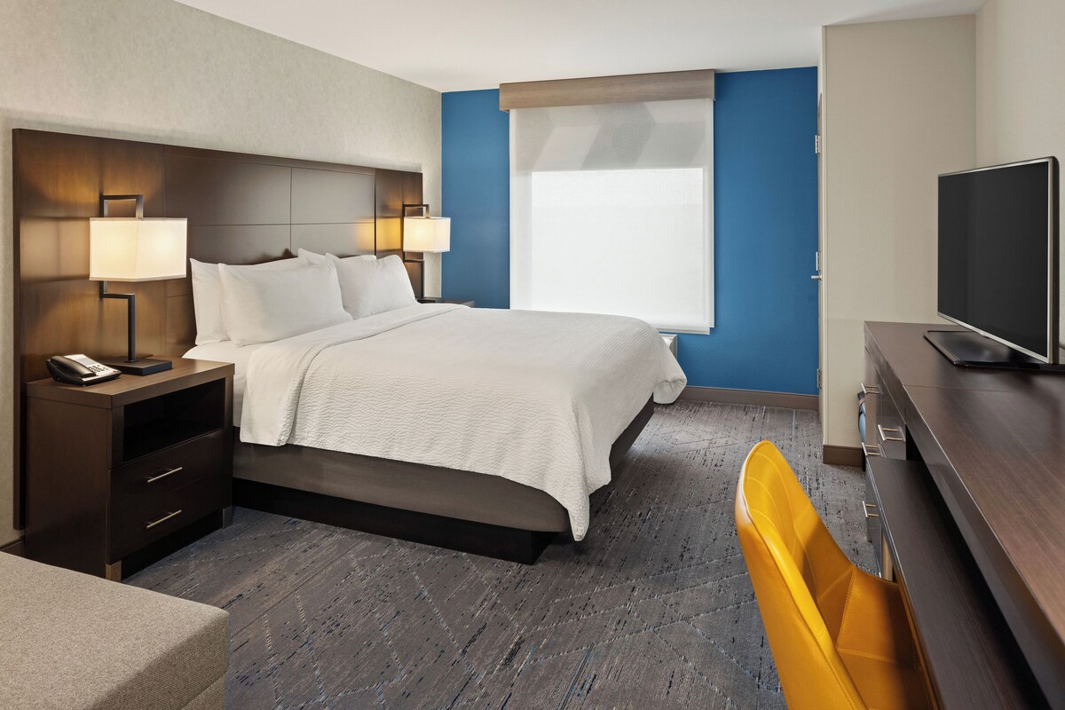 A hotel room with a bed, bedside lamps, a desk with a telephone, a television, and a chair.
