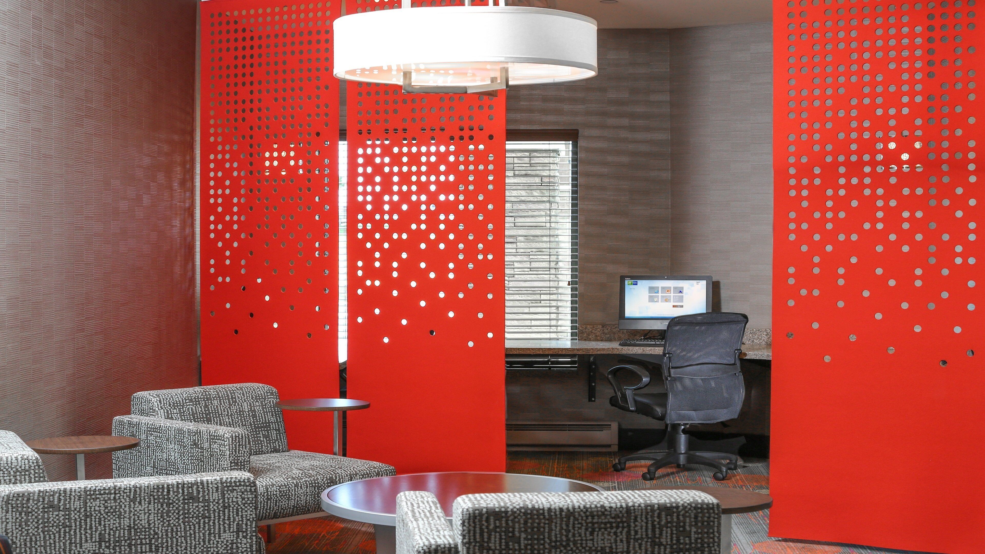 A modern office space with a round table, office chairs, a computer desk, and a red partition with holes.