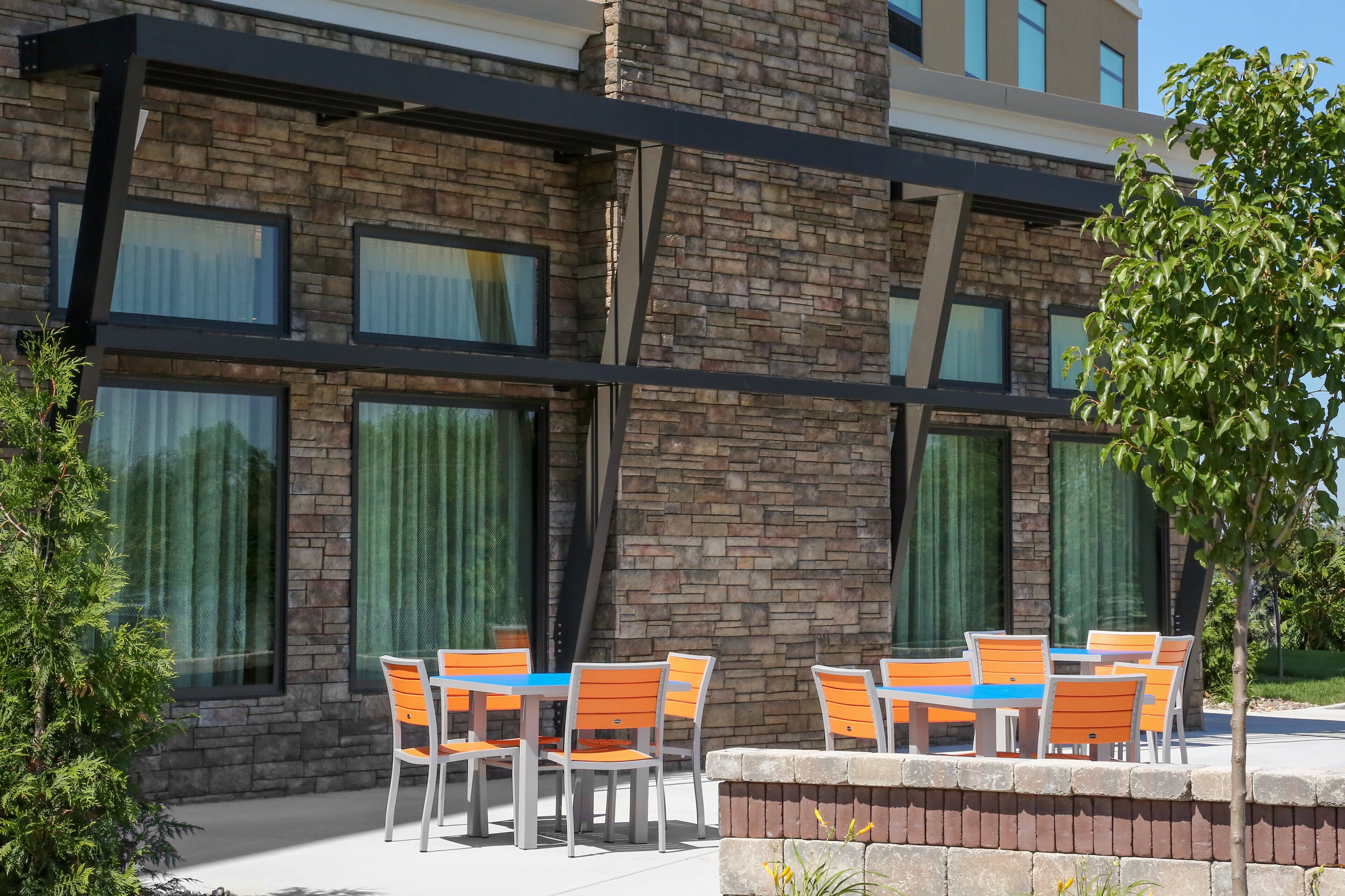 A building with a stone facade, multiple windows, and outdoor seating with orange chairs and blue tables.