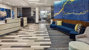 A modern hotel lobby with a reception desk, seating area, and a large map mural.