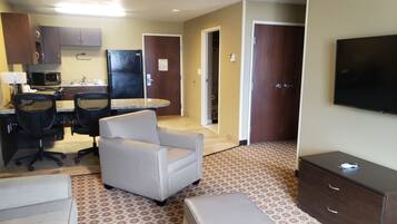 A hotel room with a kitchenette, a dining area with a table and chairs, a sofa, a TV, and a wardrobe.