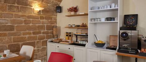 A breakfast area with a brick wall, white cabinets, a red chair, and a coffee machine.