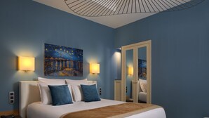 Una habitación de hotel con una cama grande, dos lámparas fijadas a la pared, un cuadro, un espejo y una mesita de noche con un teléfono.