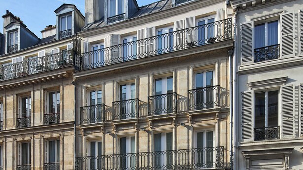 Un hotel de varios pisos con balcones, fachada verde y cielo azul despejado.
